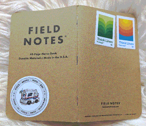 Field Notes notebook cover with a sticker on it featuring a mail truck with the text 'Field Notes Mail Day: Loved by Field Nuts Everywhere.'